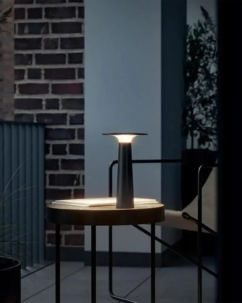 Een zwarte draagbare lamp op een ronde bijzettafel op een balkon, bij avond