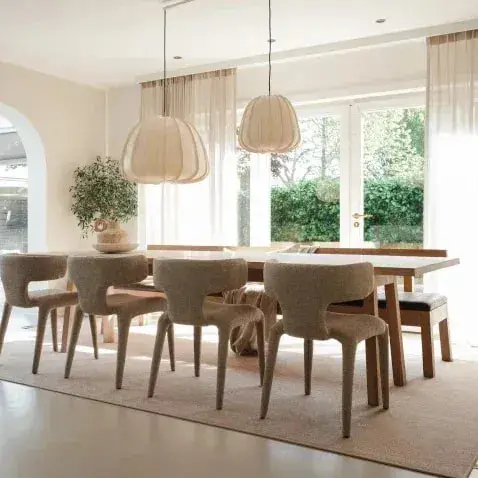 Lange eettafel onder stoffen hanglampen op een groot, licht karpet