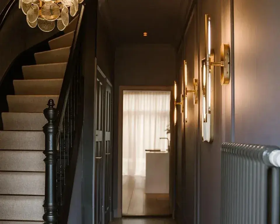 Donkere hal met een lichte traploper, messing wandlampen en een glazen kroonluchter