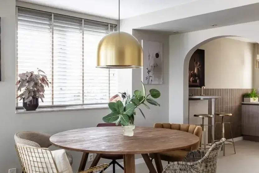 Eethoek met houten jaloezieën, een ronde tafel en een gouden hanglamp