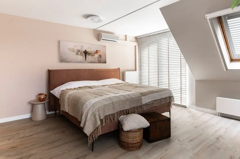 Slaapkamer onder een schuin dak met houten jaloezieën voor het raam