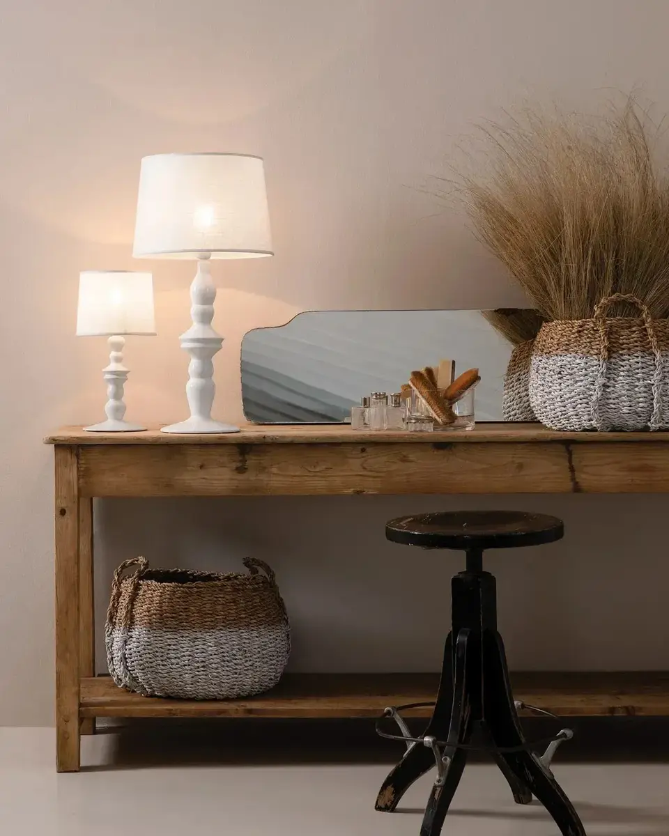 Twee witte keramieken tafellampen met een kap op een eiken wandtafel met manden, gedroogd gras en een ijzeren kruk