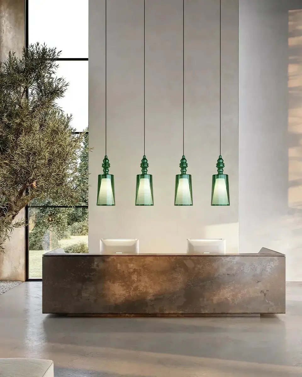 Een stenen balie onder vier groene glazen hanglampen, met een olijfboom en hoge ramen