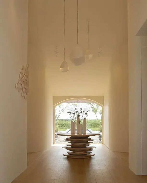 Een lichte gewelfde gang met witte hanglampen, uitkomend op een boograam