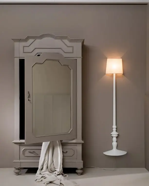Een witte staande lamp met kap naast een oude grijze kast