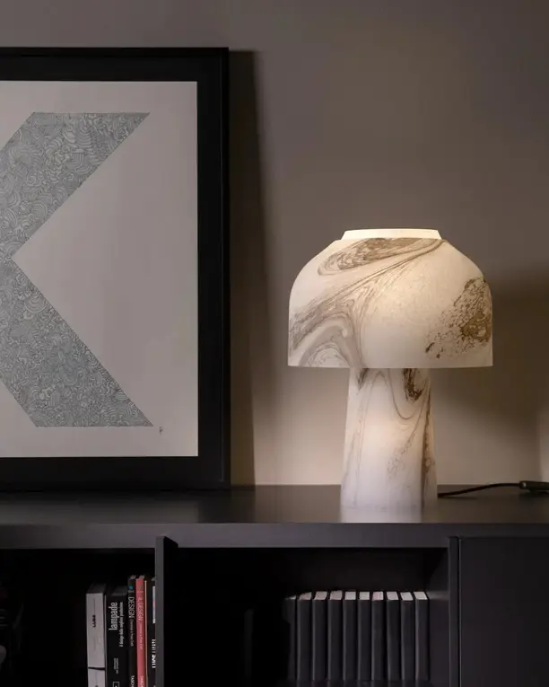 Een tafellamp van gemarmerd glas op een donkere kast voor een ingelijste letter