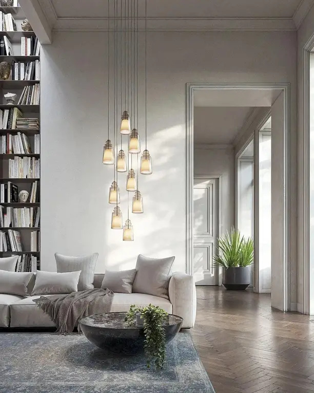 Een groep glazen hanglampen in een hoge woonkamer met boekenkast en lichte bank