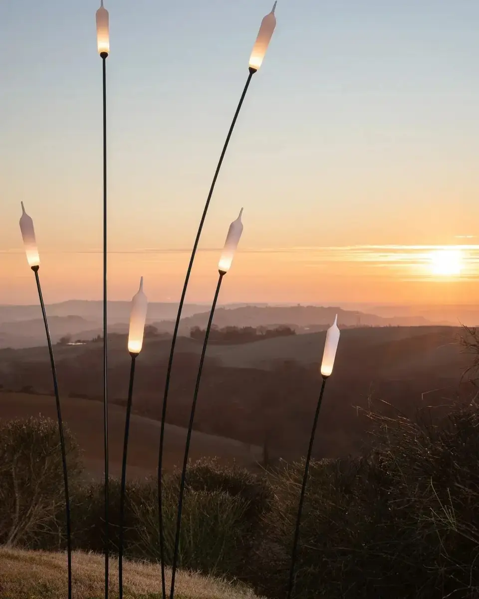 Dunne lichtstelen met witte kapjes in een heuvelachtig veld bij zonsondergang