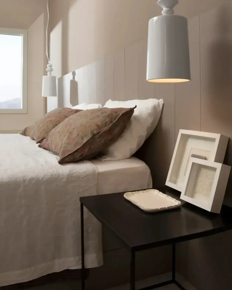 Een witte keramieken hanglamp boven een opgemaakt bed met linnen kussens