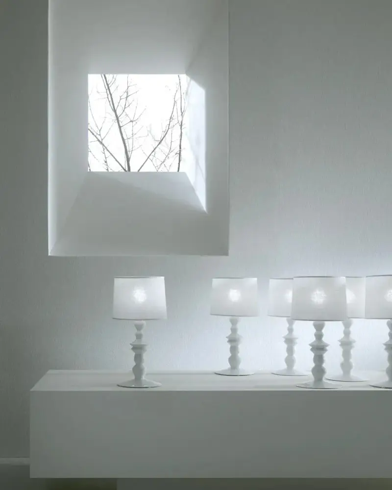 Een rij kleine witte tafellampjes op een witte bank onder een raam