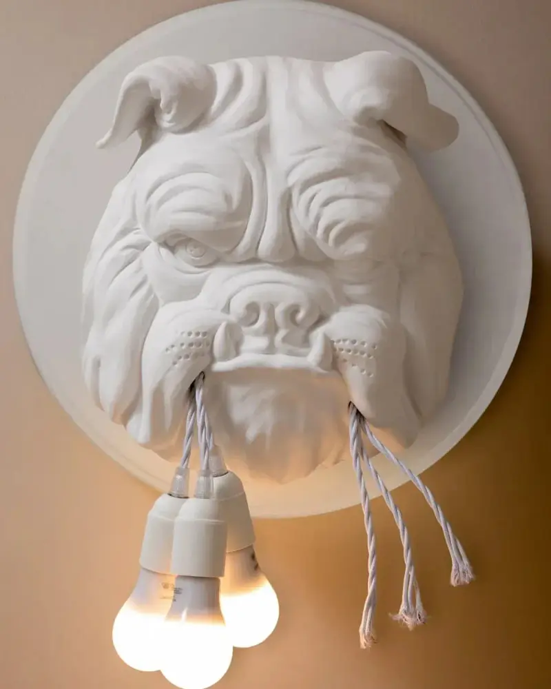 Een witte keramieken bulldogkop aan de wand met drie brandende lampjes aan snoeren in de bek