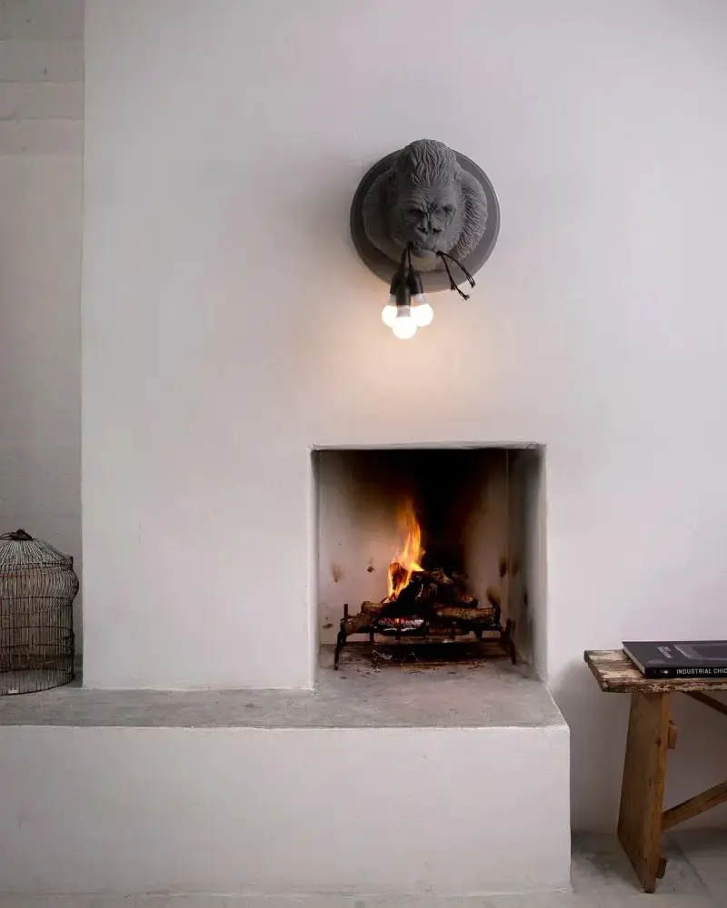 Een grijze keramieken gorillakop als wandlamp boven een open haard