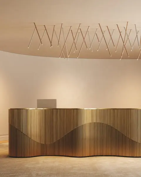 Een veld van dunne schuine hanglampen onder een golvend plafond, boven een gouden balie met ribbels