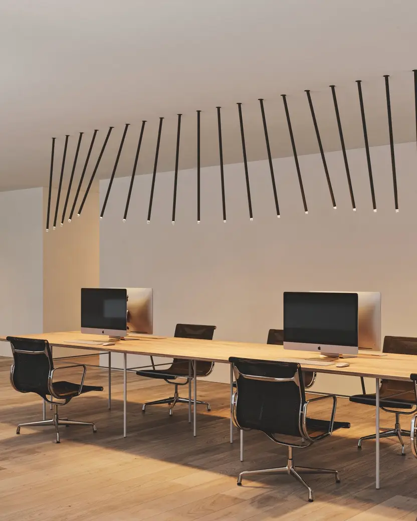 Een lange rij schuine zwarte hanglampen boven een werktafel met beeldschermen