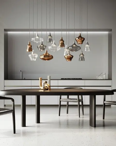 Een cluster van glazen hanglampen in koper, rook en helder glas boven een lange donkere eettafel