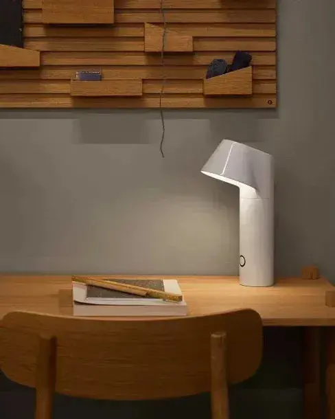 Een witte tafellamp op een houten bureau onder een wandrek
