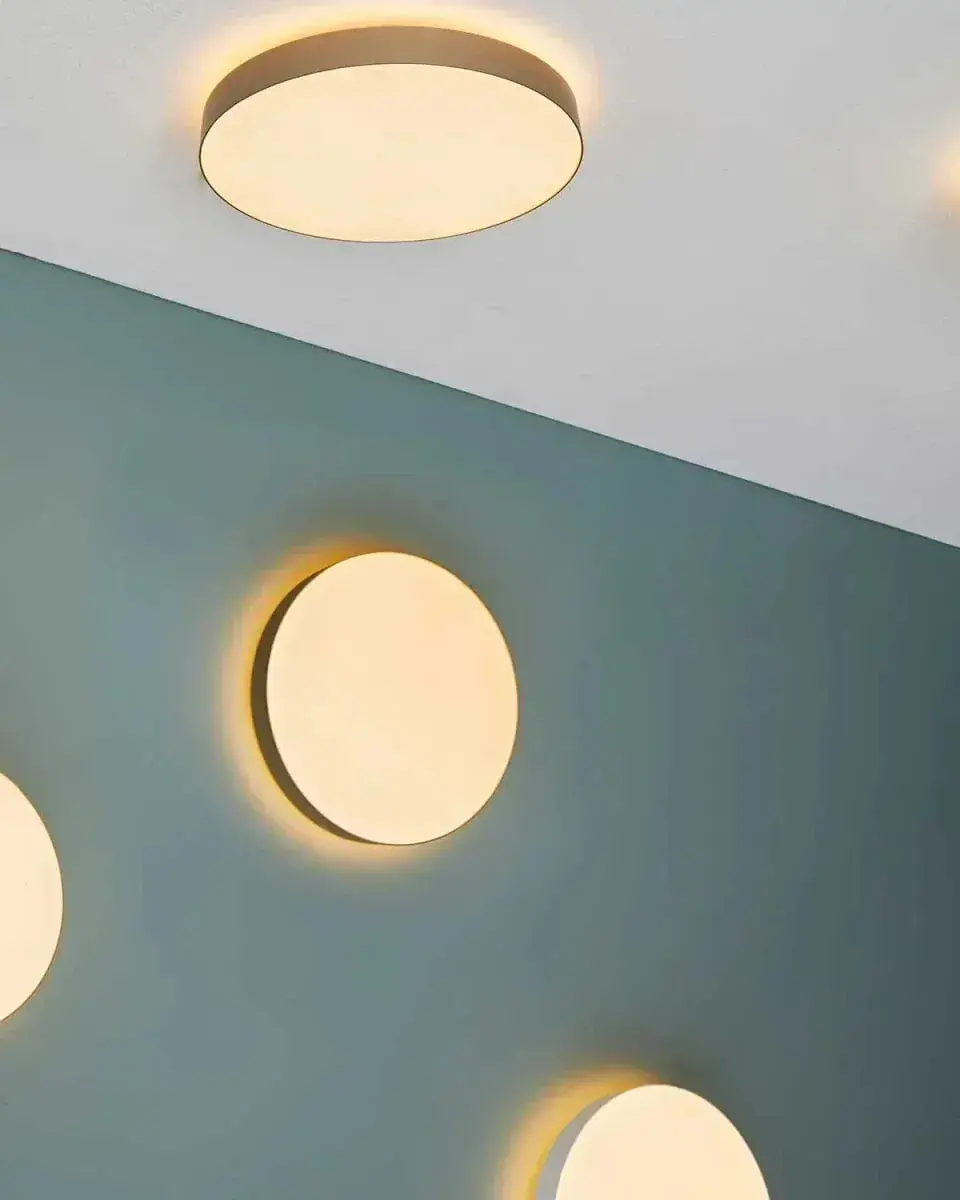 Ronde witte plafond- en wandlampen met een gouden rand op een groenblauwe wand
