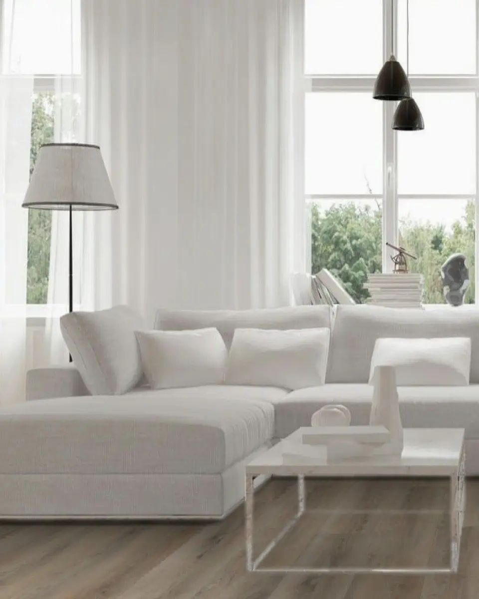 Lichte woonkamer met een witte hoekbank en een staande lamp op een brede plankenvloer in pvc
