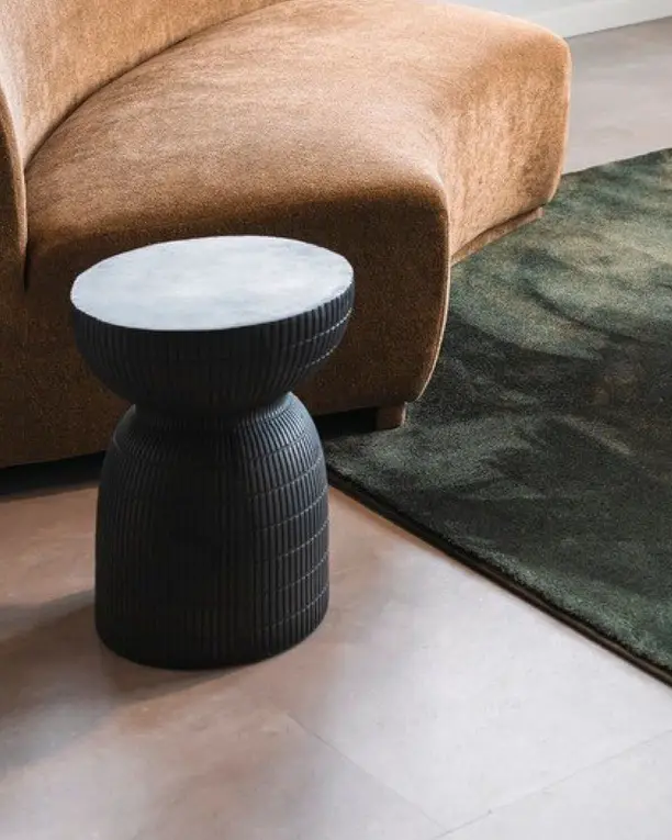 Cognackleurige bank en een zwarte bijzettafel op een tegelvloer in betonlook