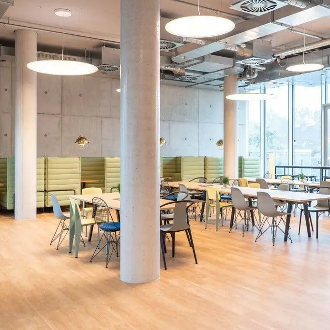 Grote ronde hanglampen boven lange tafels in een licht bedrijfsrestaurant met betonnen zuilen