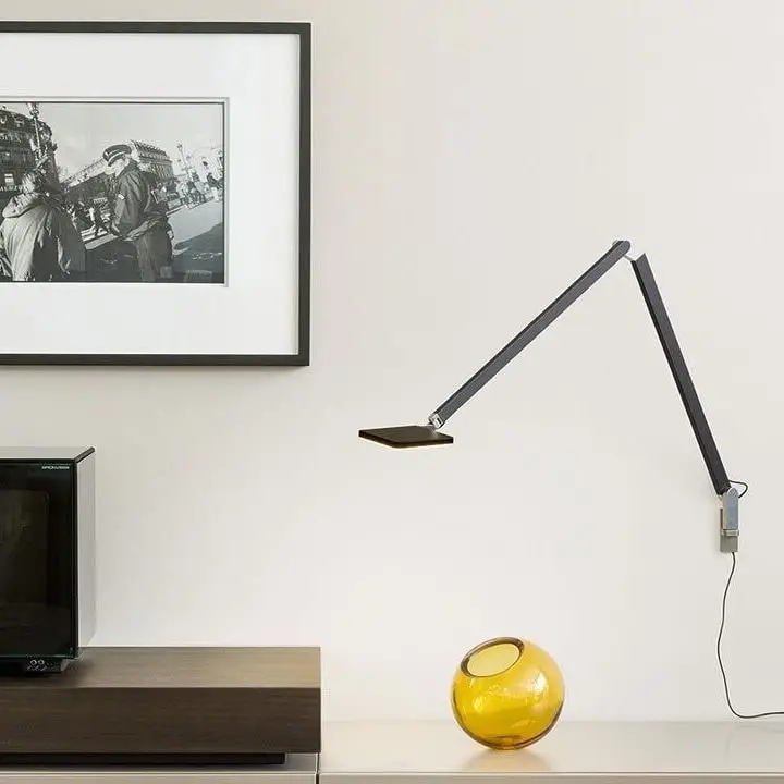 Een donkere wandlamp met een scharnierende arm boven een dressoir, naast een ingelijste zwart-witfoto