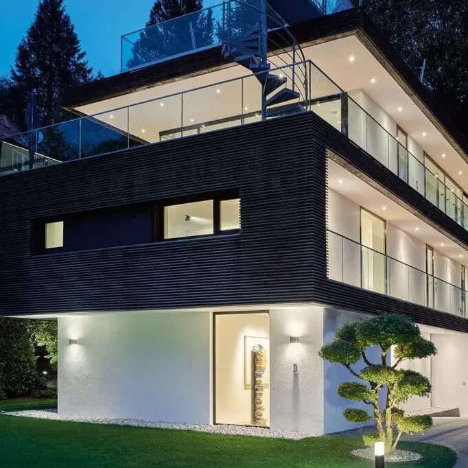 Een moderne villa bij avond, met verlichte ramen, terrassen en tuin