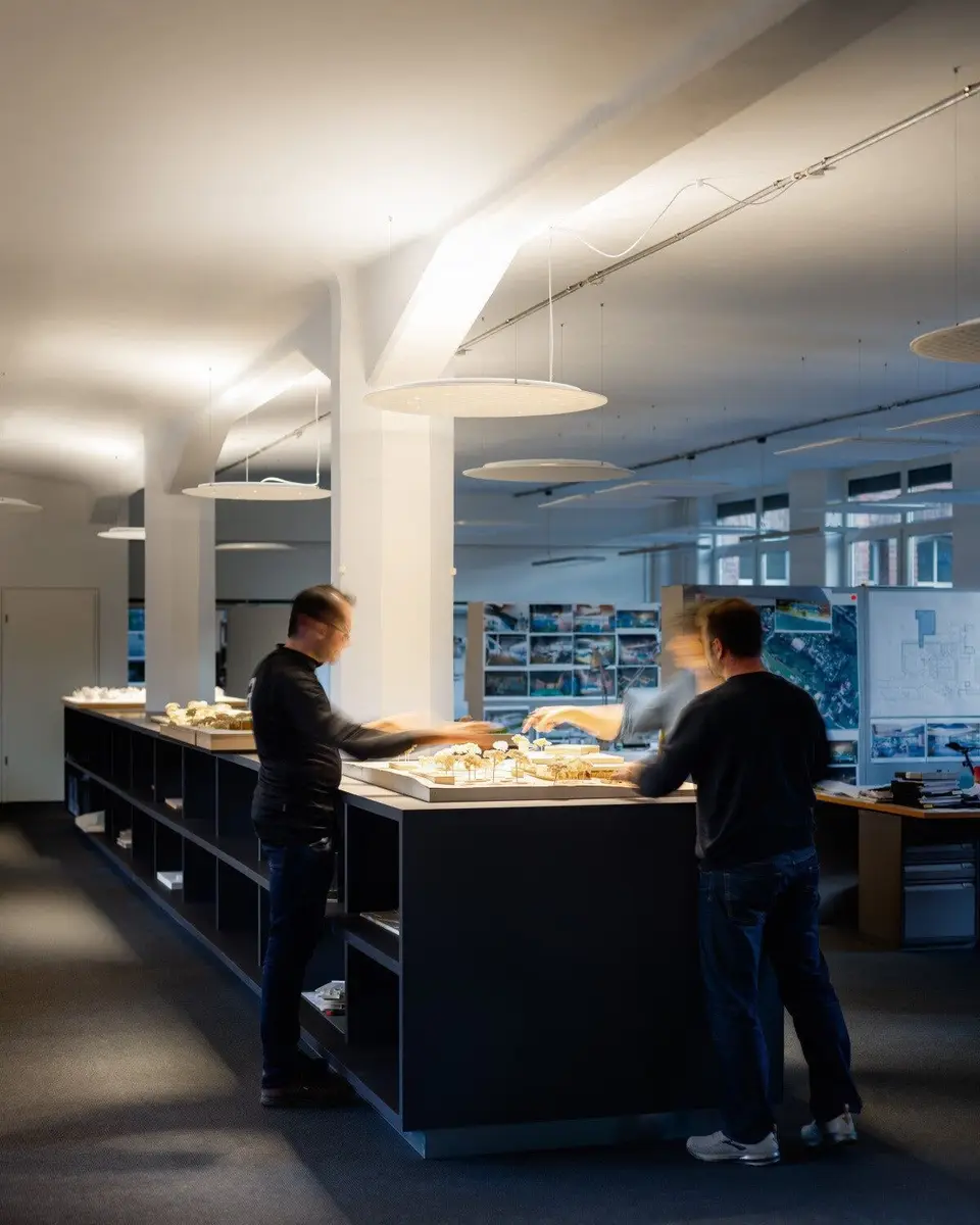 Twee mensen aan een lang werkeiland in een kantoor, onder ronde lichtpanelen aan dunne kabels
