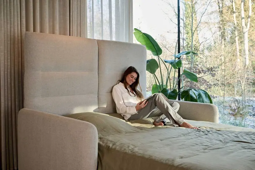 Een vrouw leest op de opengeklapte Agio tegen de hoge rugleuning, bij een raam met planten