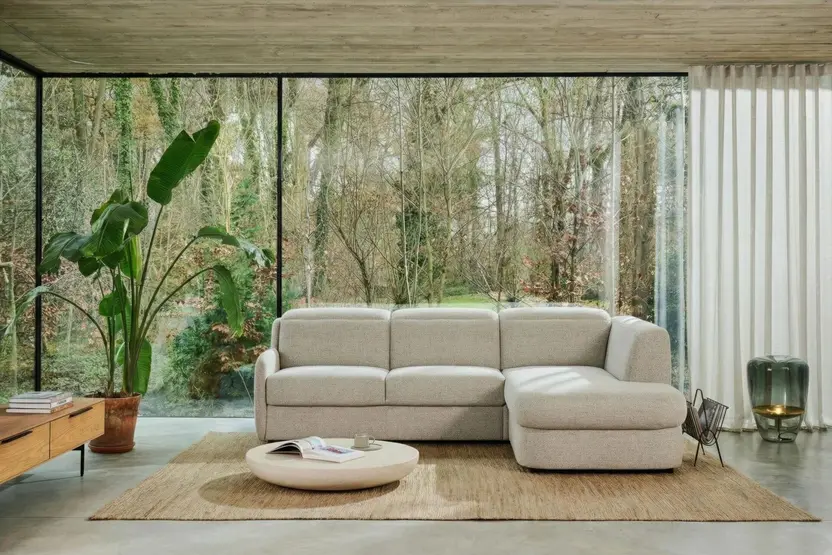 De slaapbank Vario met longchair in een glazen woonkamer aan het bos, met een ronde salontafel op een jute kleed