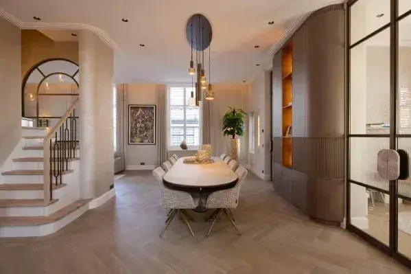 Eetkamer met een ovale tafel, een trap en een boogvenster op een lichte visgraatvloer