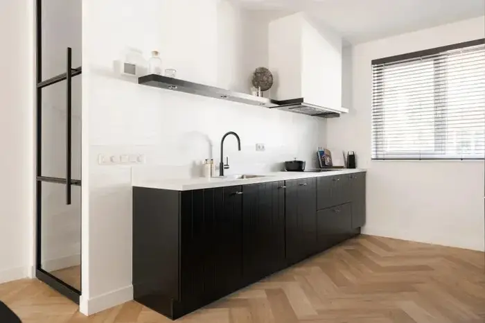 Witte keuken met zwarte fronten en een stalen deur op een visgraatvloer