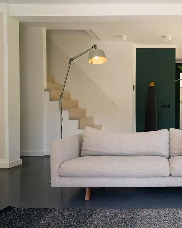 Een grijze vloerlamp met een lange arm naast een lichte bank bij een trap