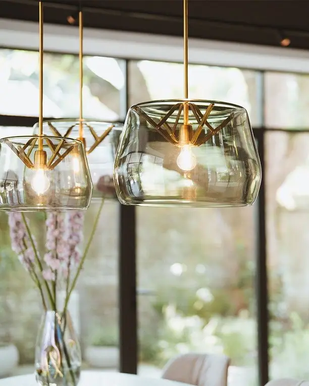 Twee hanglampen van helder glas met een messing ophanging voor een groot raam