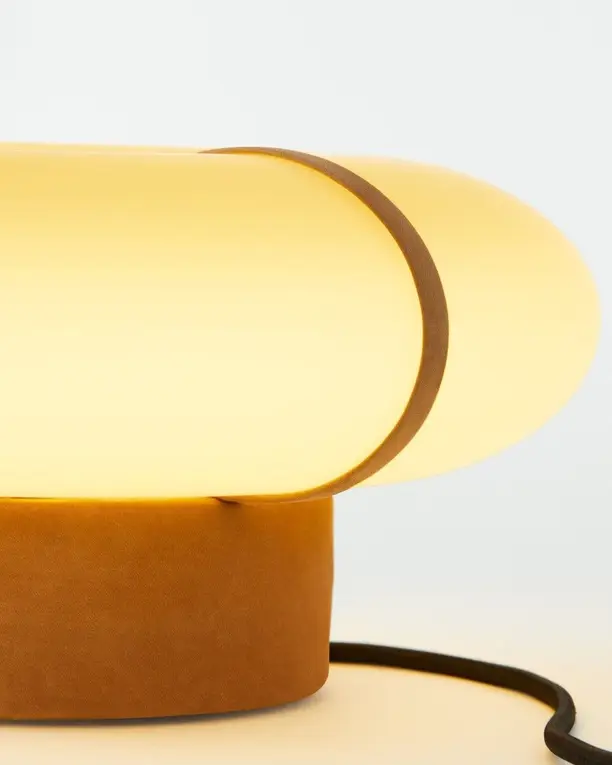 Een tafellamp van amberkleurig glas met een leren band op een terracotta voet