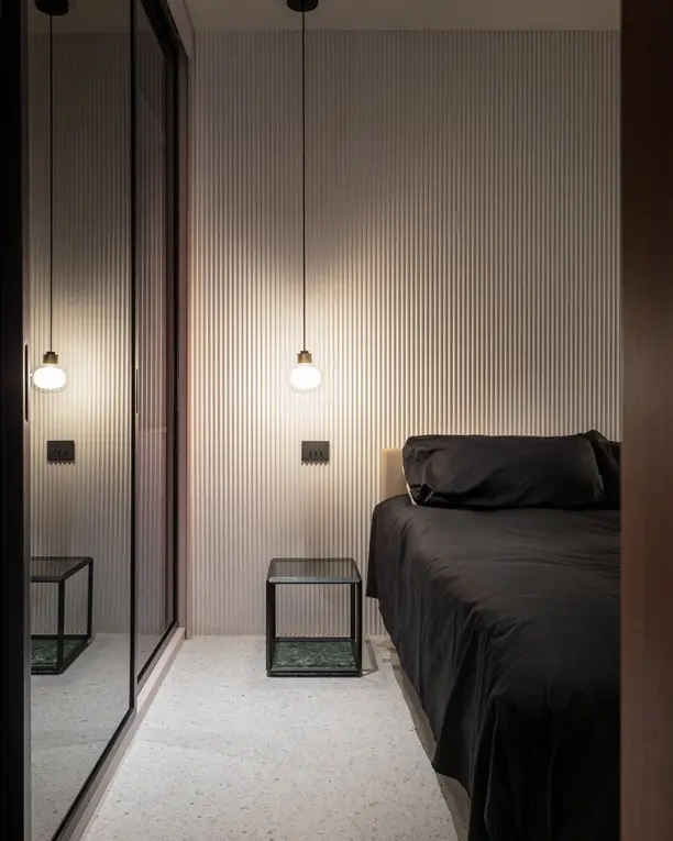 Een smalle slaapkamer met donkere wanden en twee kleine hanglampjes naast het bed