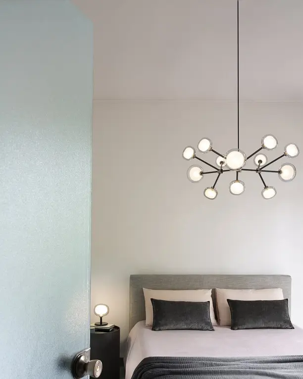 Een kroonluchter van kleine glazen bollen in een lichte slaapkamer met een grijs bed