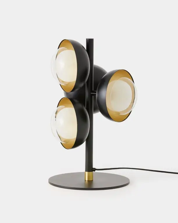 Een tafellamp met drie zwarte koepels met een gouden binnenkant en opaalglas, op een lichte achtergrond