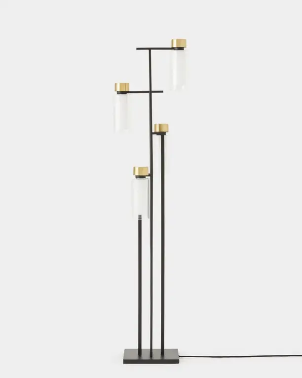 Een staande lamp met drie glazen cilinders aan een zwart frame met messing details, op een lichte achtergrond