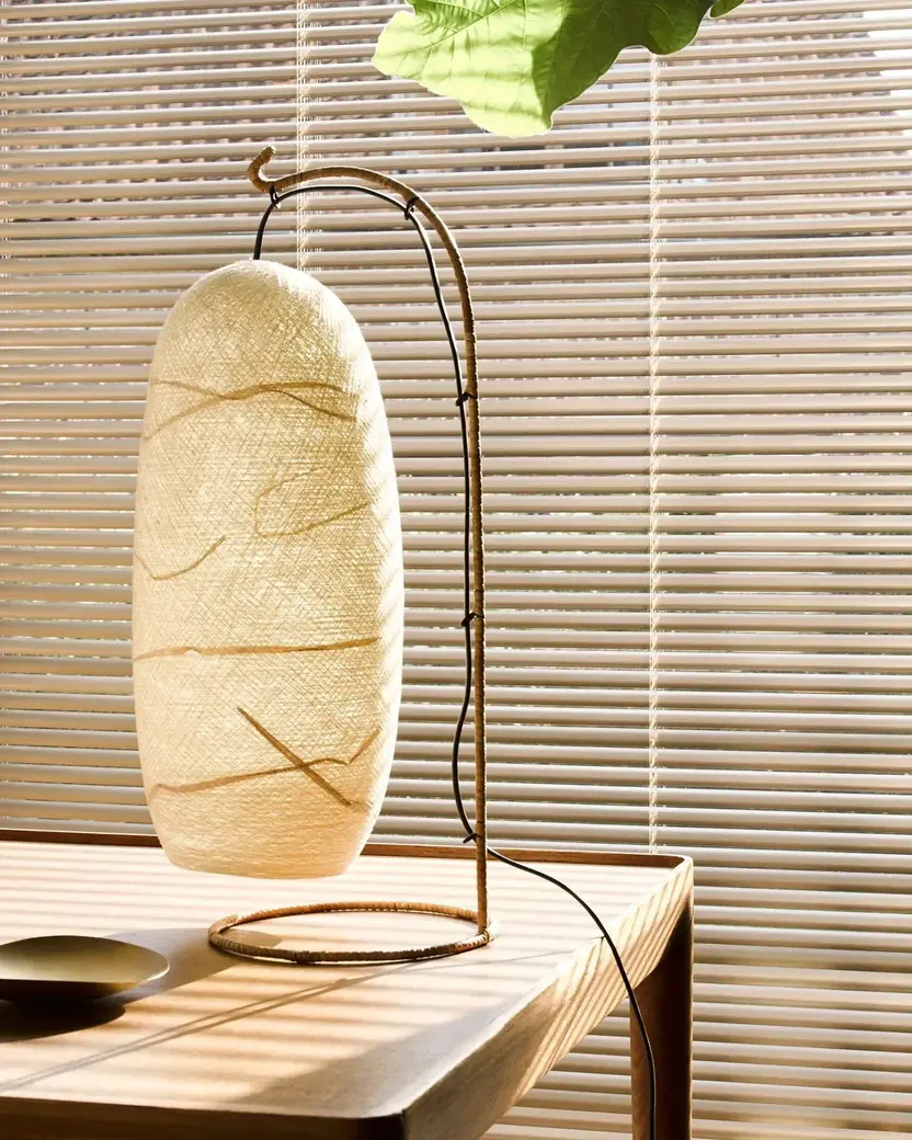 Beige aluminium jaloezie achter een papieren tafellamp op een eiken tafel