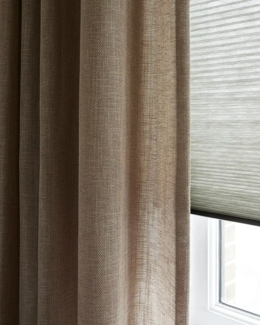 Plooien van een taupe gordijn naast een lichte plissé, van dichtbij
