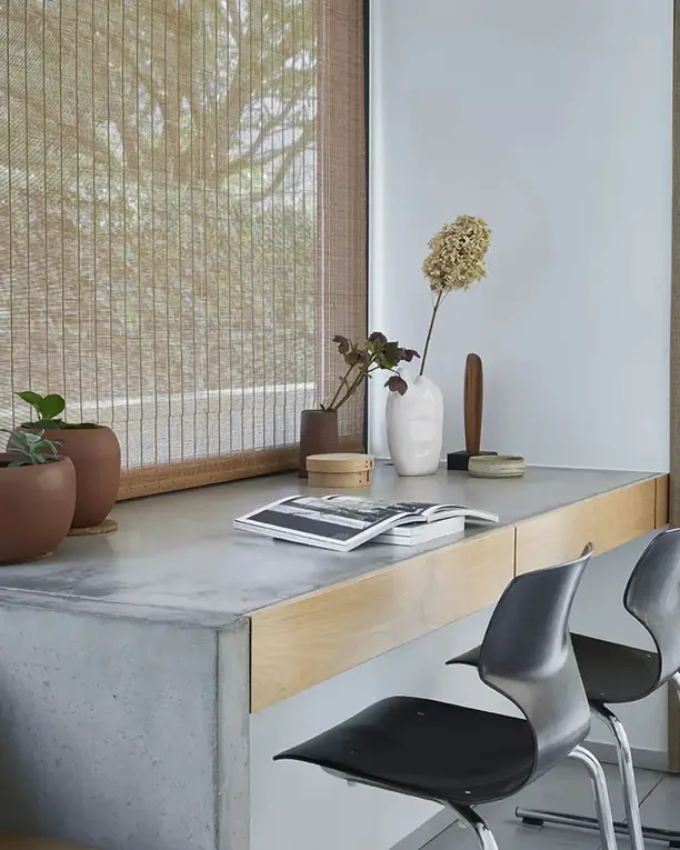 Bamboe rolgordijn boven een betonnen bureau met twee zwarte stoelen, een linnen gordijn ernaast