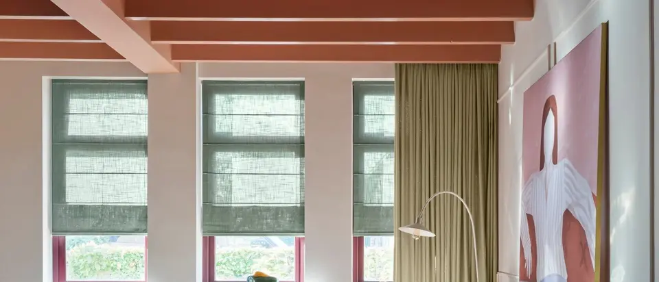 Lange kamer met een balkenplafond, drie ramen met groene vouwgordijnen en een olijfgroen gordijn