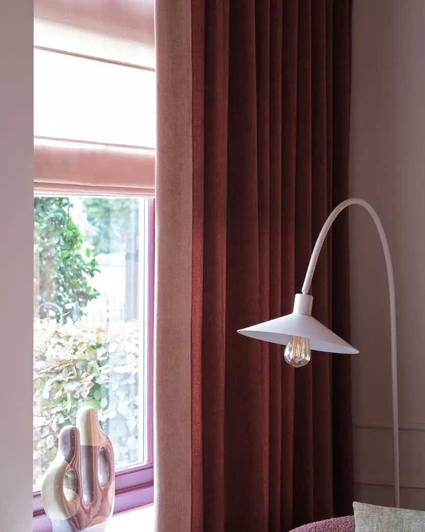 Rood gordijn met een roze vouwgordijn en een witte booglamp bij het raam