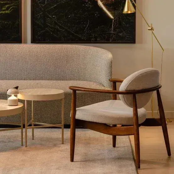 Houten fauteuil en ronde tafeltjes voor een gebogen bank op een licht karpet