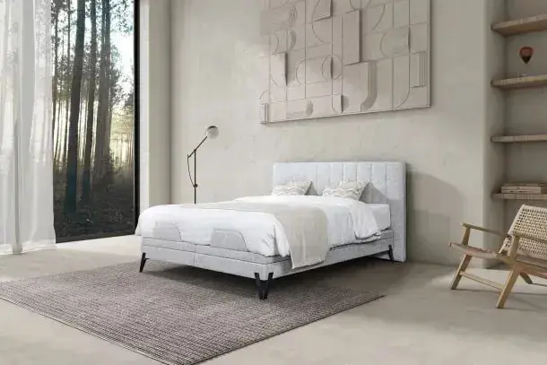 Een lichte boxspring met het hoofdbord Ember in een kamer met een raam op het bos