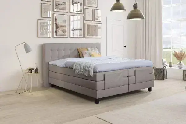 Een elektrisch verstelbare boxspring met een geruit hoofdbord in ecru, onder een wand met ingelijste foto's