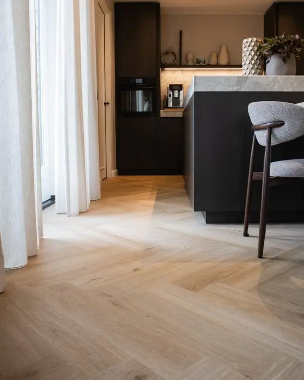 Zwarte keuken met een lichte visgraatvloer tussen linnen gordijnen