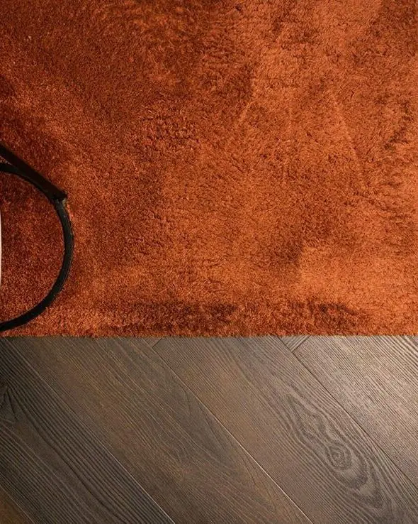Roestkleurig kleed en een rieten poef op een donkere eiken vloer