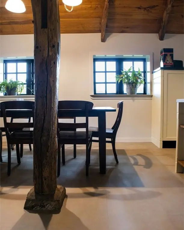 Boerderijkamer met een eiken balk en een eettafel op een tegelvloer in betonlook
