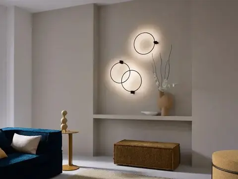Drie ronde lichtringen aan een taupe wand boven een nis, naast een blauwe bank en een boograam